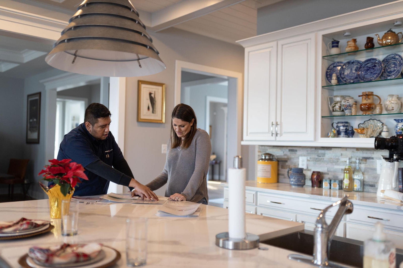 bell-tower-electrician-consulting-with-homeowner A professional electrician from Bell Tower Electric reviewing paperwork and project plans with a female homeowner on a kitchen island.