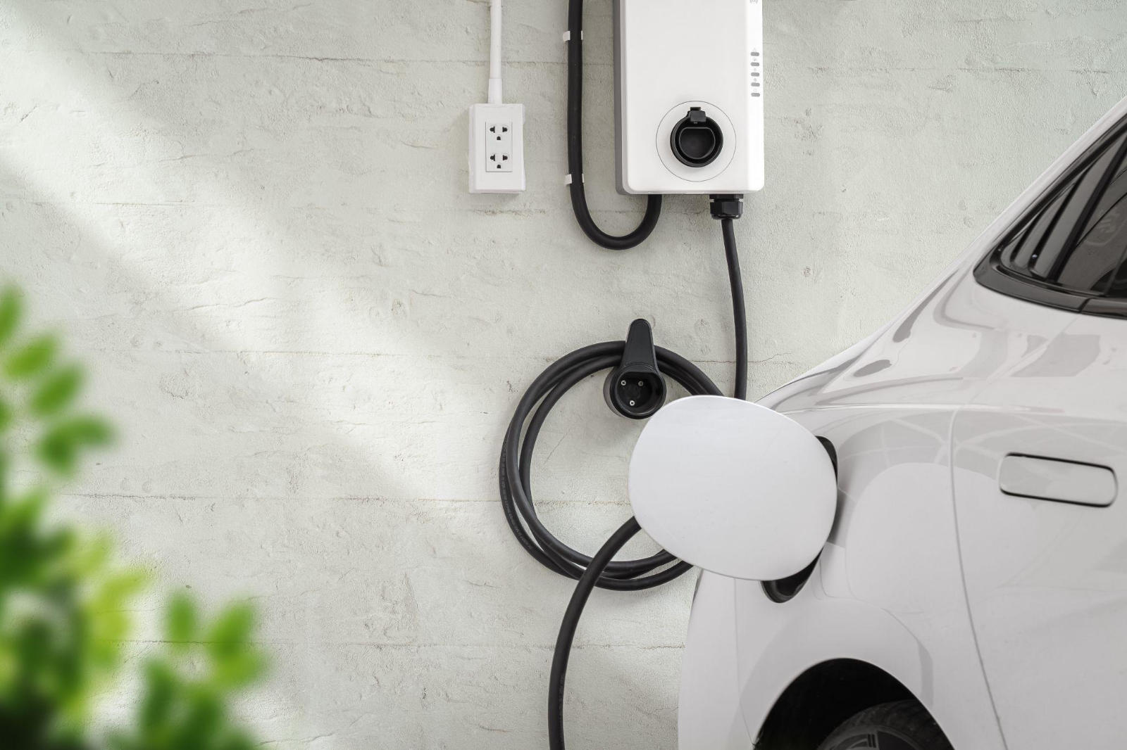 A wall-mounted Level 2 EV charger and neatly coiled charging cable connected to a white electric vehicle.